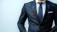 Professional businessman wearing dark suit, white shirt and blue tie against light background, cropped view showing formal attire details and elegant style.