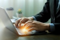Professional businessman hands typing on laptop keyboard with glowing light effect in modern office workspace for business and technology concepts.
