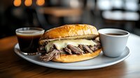 Juicy roast beef sandwich with melted cheese on fresh bun served with espresso and coffee on white plate against dark restaurant background.