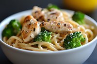 Creamy fettuccine pasta with grilled chicken breast strips, steamed broccoli florets and black pepper in white ceramic bowl, close-up food photography.