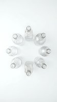 Empty clear glass bottles arranged in circular pattern on white background for packaging design and product mockups.