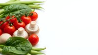 Fresh organic vegetables including cherry tomatoes, mushrooms, spinach and green beans arranged on white background for healthy cooking and nutrition.
