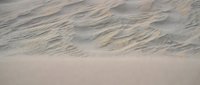 Gentle ocean waves washing over sandy beach shore creating natural water patterns and textures. Peaceful coastal scene with soft foam and ripples on wet sand.