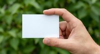 Hand holding blank white business card mockup against green foliage background for branding and corporate identity design templates.