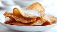 Golden crispy crepes dusted with powdered sugar on white plate, close-up view. Sweet dessert for breakfast or brunch.