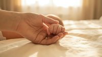 Tender moment of adult hand gently holding baby's tiny fingers in warm golden sunlight, symbolizing love, protection, care, family bond and new life beginning.