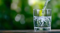 Fresh clean water pouring into clear glass with bubbles against blurred green nature background for hydration and wellness concepts.