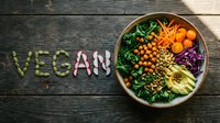 Colorful vegan Buddha bowl with kale, avocado, chickpeas, carrots, and cabbage on rustic wood, with the word VEGAN spelled in seeds.