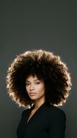 Young African American woman with voluminous curly afro hairstyle wearing black blazer against dark background for beauty and fashion concepts.
