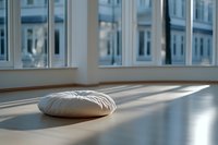 Round white meditation cushion on wooden floor with natural sunlight casting long shadows through windows, creating peaceful zen atmosphere in minimalist room.