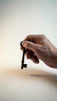 Male hand holding vintage black key against neutral background symbolizing access, solutions, and unlocking opportunities for business concepts.