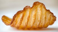 Crispy golden ridged potato chip with distinctive wavy pattern captured in macro photography showing detailed texture and warm lighting on neutral background.