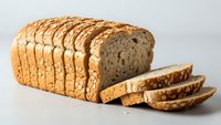 Freshly sliced whole grain bread loaf with seeds on neutral background, perfect for healthy eating and bakery concepts.