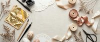 Flat lay crafting workspace with dried flowers, ribbons, scissors and decorative elements on neutral background for creative projects and handmade designs.