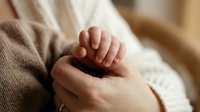Tender moment of parent holding newborn baby hand in soft natural light showing love bond and care between mother and child in cozy home setting.