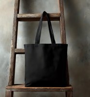 Black canvas tote bag hanging on rustic wooden ladder against textured wall, minimalist eco-friendly shopping accessory for everyday use.