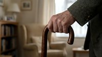 Senior man's hands gripping wooden walking cane in cozy home interior, elderly care and mobility assistance concept for healthcare materials.