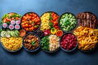 Colorful bowls filled with diverse foods including grilled meat, french fries, fresh vegetables, corn, rice and berries arranged on dark background for restaurant menu or catering.
