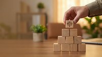 Hand placing wooden cube with tree symbol on pyramid of blocks representing growth, sustainability and environmental business concepts on desk.