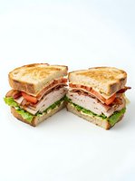 Toasted sandwich halves filled with sliced turkey, crispy bacon, fresh lettuce, and tomato on white background. Suitable for restaurant menus, food delivery apps, and culinary marketing.