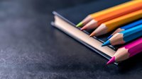 Colorful wooden pencils arranged on dark textured background with dramatic lighting and shallow depth of field, showcasing vibrant art supplies for creative projects.