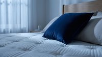Dark blue pillow on white bedding in modern bedroom with natural light from window, suitable for home decor and interior design projects.