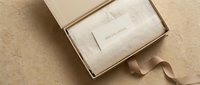 Elegant gift box with white tissue paper and special offer card, tied with satin ribbon on beige stone surface for luxury retail packaging.