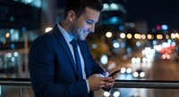 Professional businessman using smartphone at night in urban city with bokeh lights background for business communication and technology concepts.