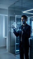 Professional businessman interacting with futuristic holographic interface displaying data analytics in modern glass office environment.