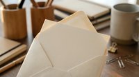 Blank kraft paper envelope opened on wooden desk with vintage books, pen holder, and coffee mug creating rustic workspace atmosphere for correspondence.
