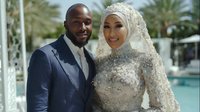 Happy African American Muslim couple in elegant wedding attire smiling together at luxury resort with palm trees and pool in background for celebration.