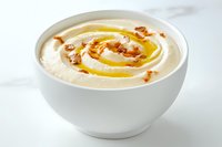 Creamy hummus served in white bowl with olive oil drizzle and crispy fried onion garnish on marble surface, traditional Middle Eastern appetizer.