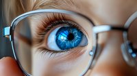 Close up macro shot of bright blue eye with long eyelashes seen through transparent eyeglasses lens, showing reflection and clarity of vision in modern optical wear.