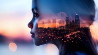 Double exposure portrait of young woman silhouette combined with vibrant cityscape at sunset showing illuminated skyscrapers and urban lights against orange sky.