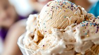 Creamy vanilla ice cream scoops with colorful sprinkles in white bowl, close-up view showing smooth texture and festive rainbow decorations for dessert concept.