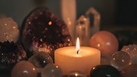 Burning candle surrounded by decorative stones and crystals creating warm ambient lighting for meditation, spa treatments, and relaxation rituals.