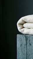 Rolled cream towels stacked on wet concrete pedestal against dark background, conveying spa, wellness and bathroom hygiene concepts for hospitality and lifestyle design projects.
