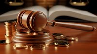 Wooden gavel with golden coins and open law books on desk representing legal fees, court costs, financial justice and attorney expenses in litigation.