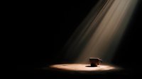 Solitary coffee cup illuminated by dramatic spotlight beam against dark background, creating moody atmospheric scene for conceptual or advertising use.