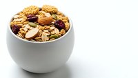 Healthy breakfast granola with nuts, dried fruits and oats in white ceramic bowl on clean background for nutrition and wellness concepts.