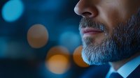 Close up profile of mature businessman with gray beard against blurred city lights background, professional corporate portrait in moody blue tones.