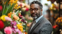 African American mature businessman with glasses and beard shopping at colorful flower market, selecting fresh blooms for special occasion or gift.