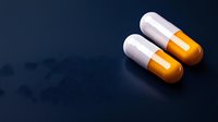 Two white and orange medical capsules on dark reflective surface with dramatic lighting, pharmaceutical concept for healthcare and medicine advertising.