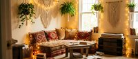 Cozy bohemian living room interior with macrame wall hangings, hanging plants, patterned cushions, warm string lights and wooden furniture for home decor.