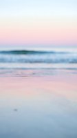 Serene coastal landscape at dawn with soft pink and blue tones, gentle waves rolling onto sandy shore, peaceful seaside atmosphere for travel and wellness designs.