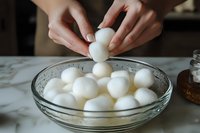 Fresh mozzarella balls being placed into glass bowl filled with water, hands adding soft cheese for cooking preparation and culinary use.