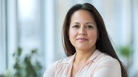 Confident Asian businesswoman with long dark hair smiling at camera in modern office setting. Professional portrait showing warmth and leadership qualities.