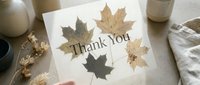 Thank you card with dried autumn maple leaves on neutral beige background, held by hand, cozy fall aesthetic for seasonal greeting design.