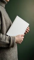 Person in gray sweater holding blank white hardcover book against green background for mockup and design projects.