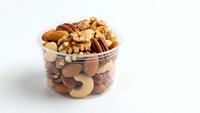 Mixed nuts and dried fruits in glass bowl on white background isolated for healthy snacking and cooking ingredients.